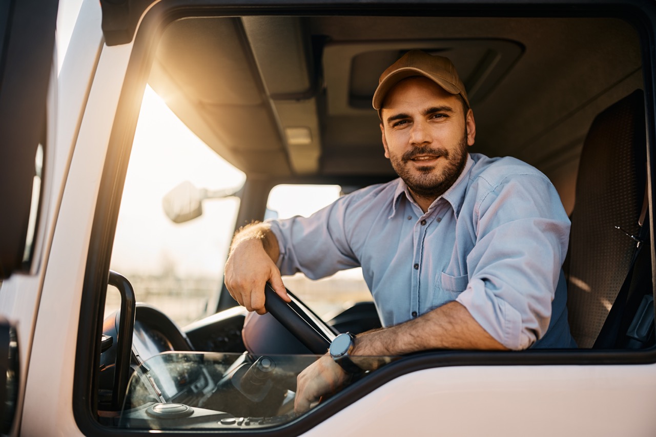 Young truck driver behind steering wheel in vehicle cabin looking at camera.